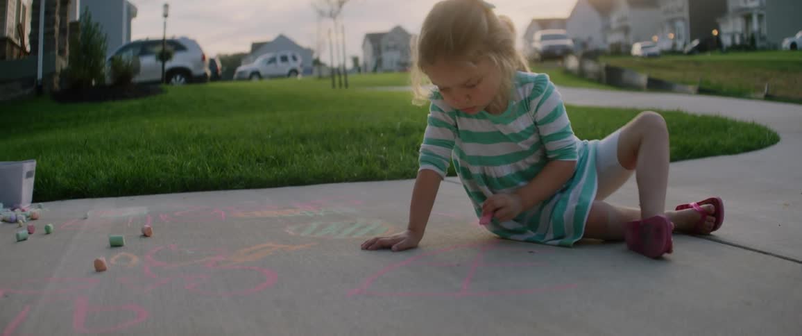 A child is drawing with chalk on the driveway