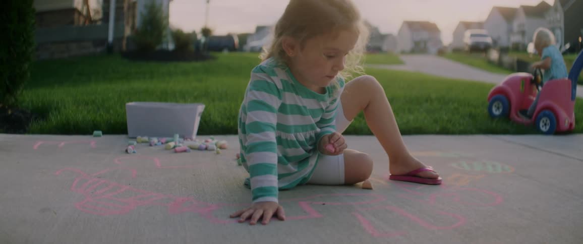 A little girl is drawing on the ground with chalk