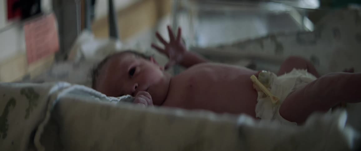 A baby is moving its arms as it lays in a crib in daylight