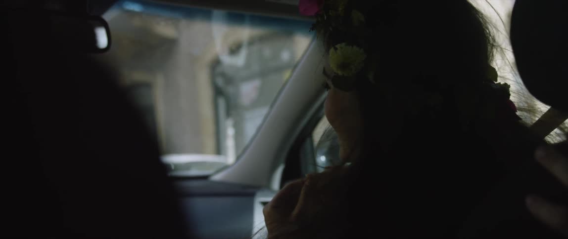 A woman with flowers in her hair smiles and turns away