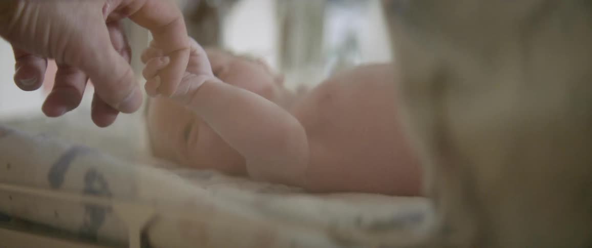 A baby holds a person's finger from the crib