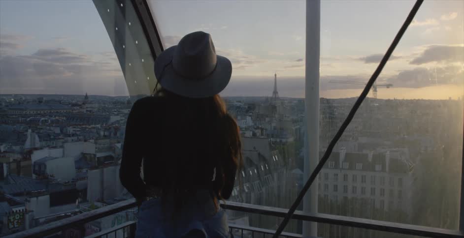 A woman is standing on a balcony looking over a city at sunset