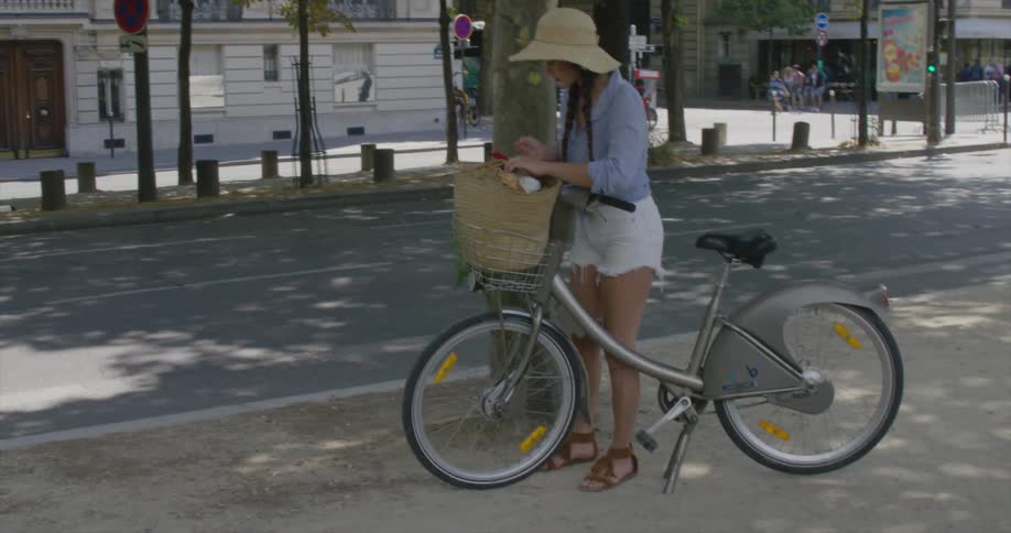 A woman places a bag in a bicycle basket while city traffic drives by
