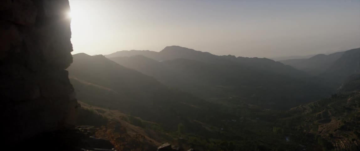 The sun comes out from behind a rock near a valley