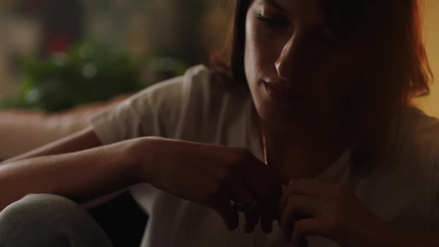 A woman sitting in a room playing with her chain with plants in the background
