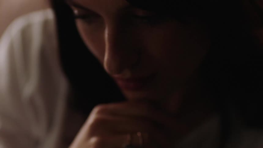 A woman leans forward pushing her hair back from her face as she thinks and has a flashback