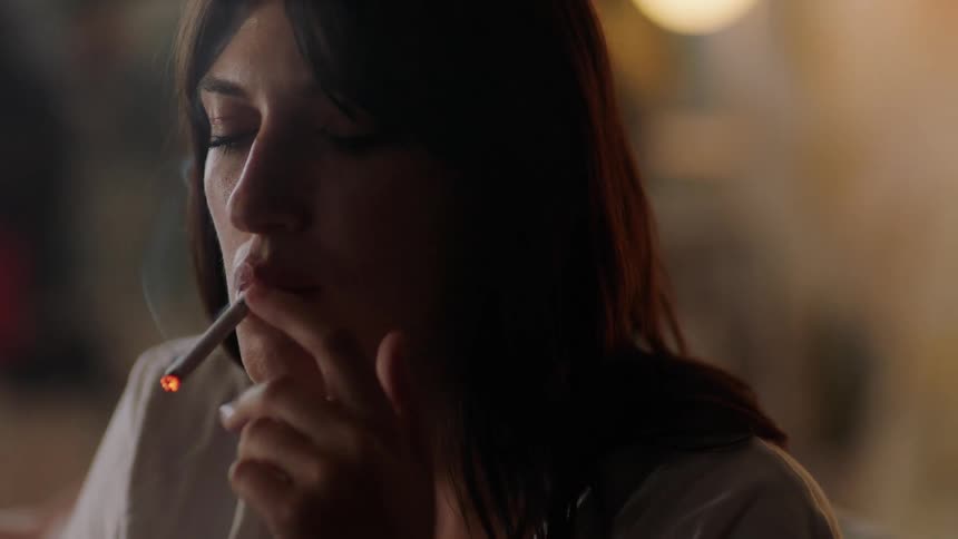 A woman lights a cigarette using a lighter before exhaling a cloud of smoke