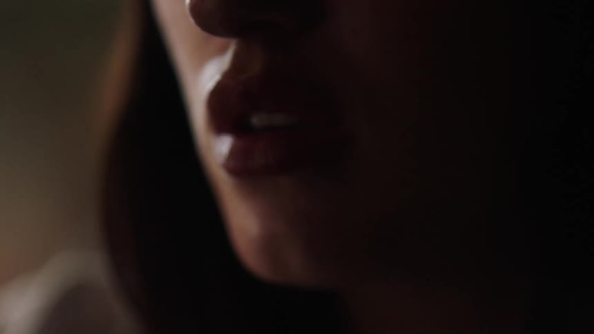 A woman smokes a cigarette, close-up, exhaling smoke from her lips.