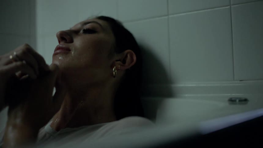 A woman lifts her head out from under the water in the bathtub and hugs her arms over her chest