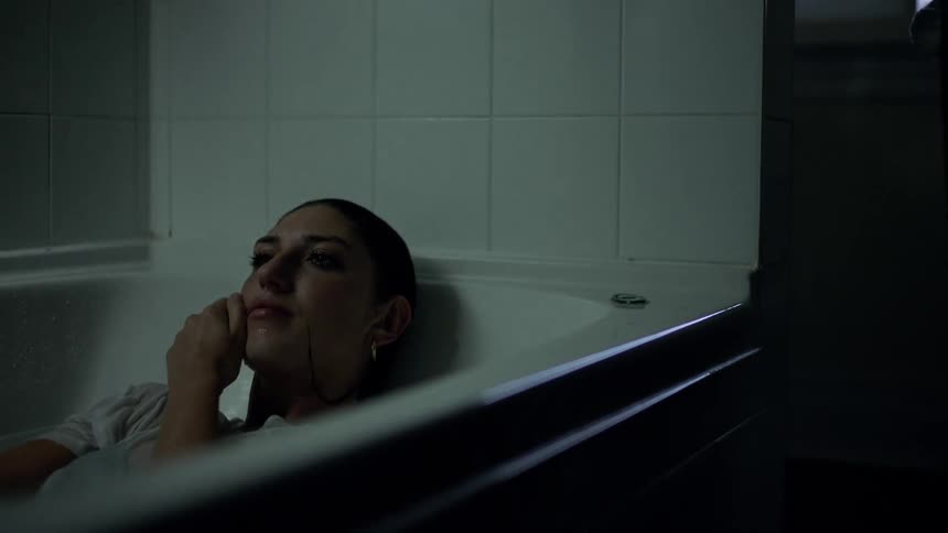 A woman in her clothes lies in a bathtub crying
