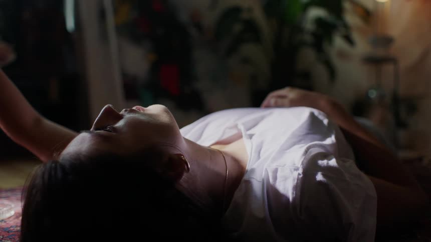 A young woman laying on the floor staring at the ceiling, blocking the sunlight from her eyes.