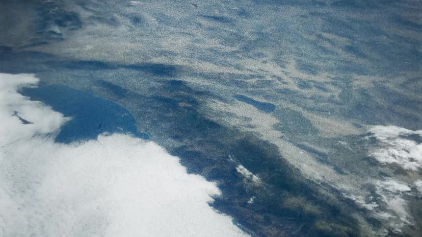 Clouds cover water and terrain in high altitude aerial shot