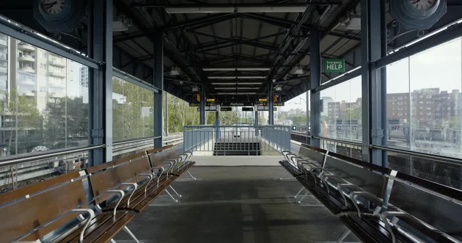 A train platform with benches and pillars with buildings and the sky in the background