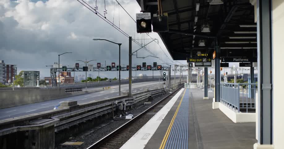 Traffic flows along street paralleling tracks across from empty transit station