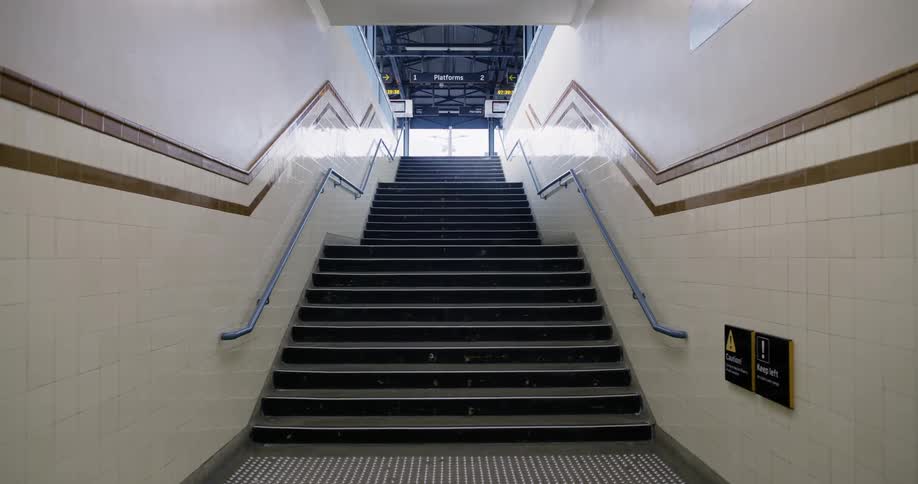Empty staircase leads past sign providing directions to platforms to glass doors in transportation hub