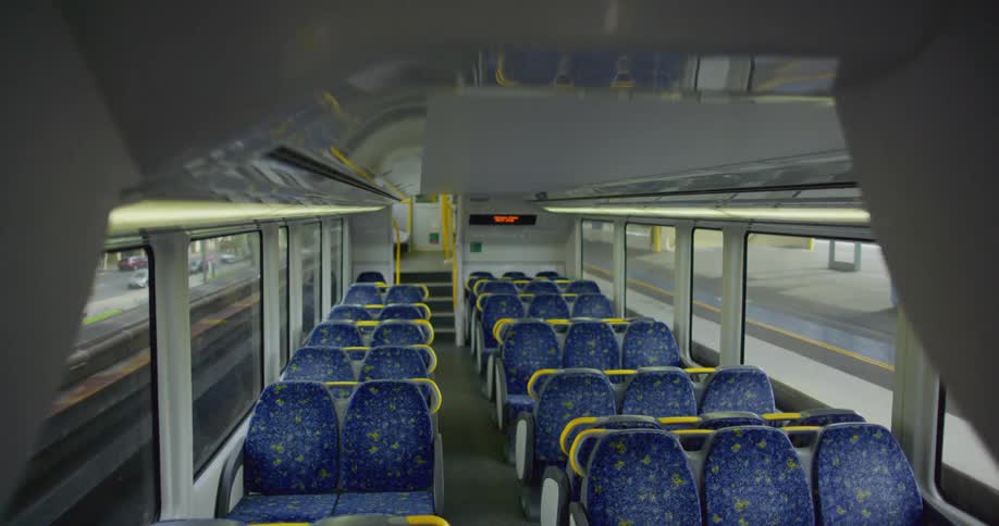 An empty train stopping at a train station with a person standing on the platform