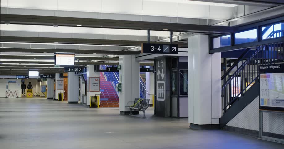 A brightly lit commuter train station is empty of people and one of its elevators begins to move