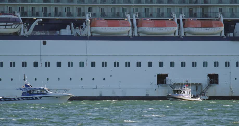 Two boats on the ocean with waves next to a large ship