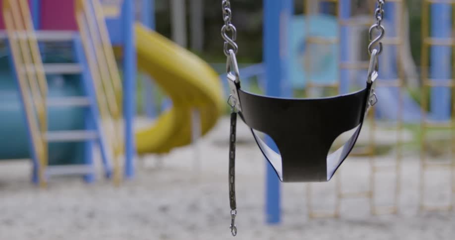 An empty baby swing in an empty playground with colorful slides and monkey bars