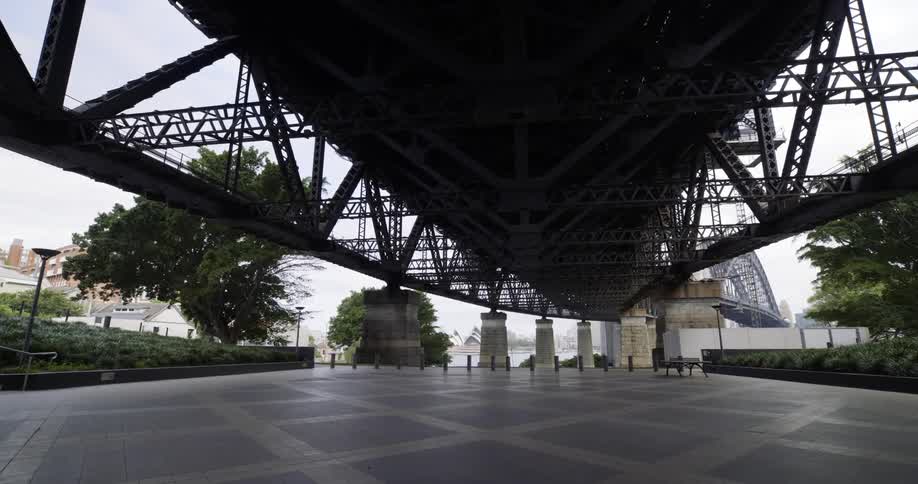 Underneath a bridge with a bench and pillars with a opera house and the sky in the background