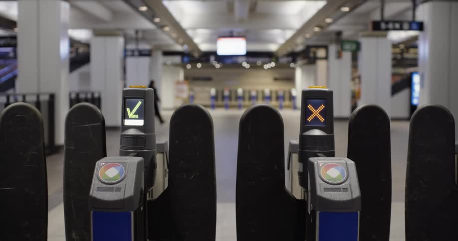 A train station turnstile in a train station with people walking by in the background