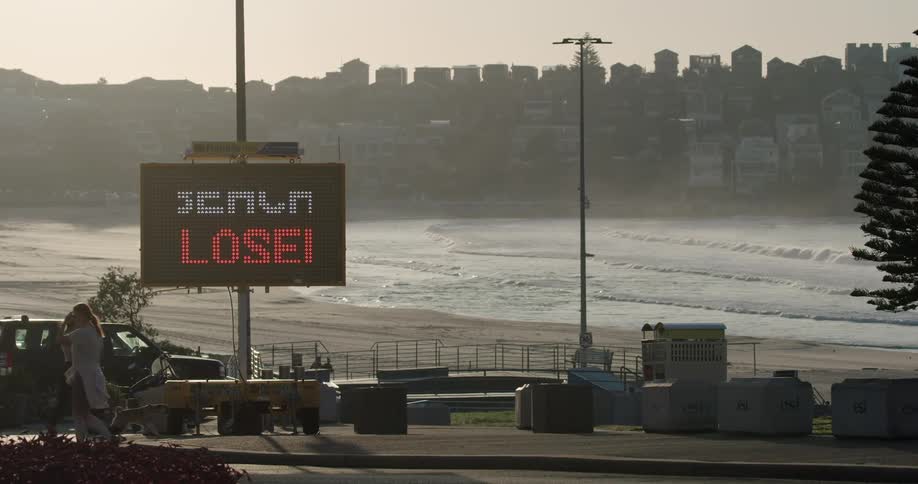 Pedestrians walk near a closed beach in a city