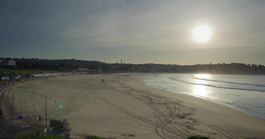 Many people stroll along a paved walking path that borders an pleasant but completely empty sandy beach