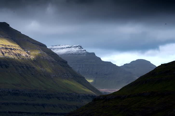 Dark clouds pass overhead above a jagged range of mountains and the valleys in between