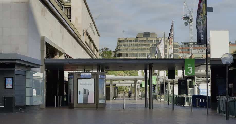 Pedestrians walk alot wide walkway near buildings with advertising displays and covered path labeled warf