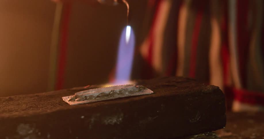 A person with a blowtorch putting flame onto a piece of metal as it rotates on a stone