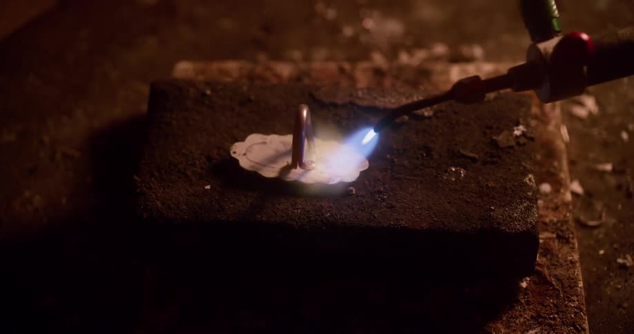 A blowtorch putting flame to a piece of metal on a stone