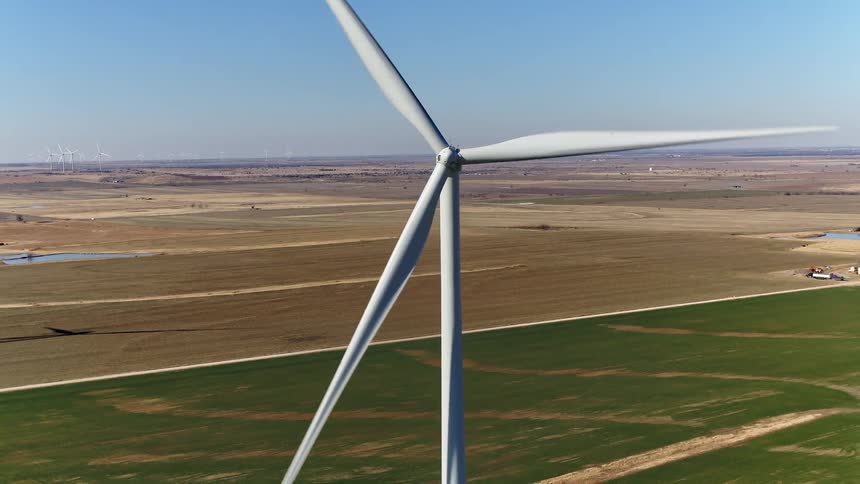 A wind turbine on a wind turbine farm on a grassy plain with the sky and clouds in the background