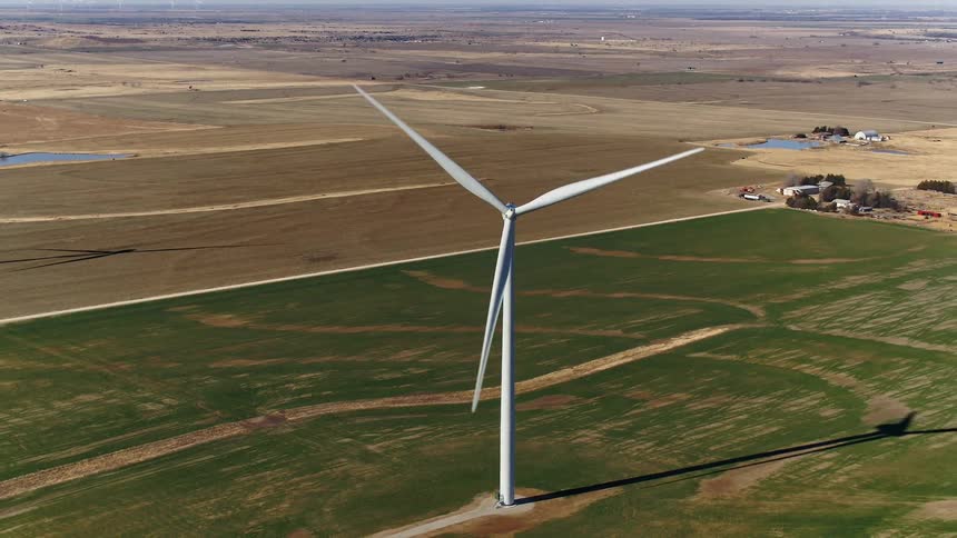 A tall windmill for harnessing wind power has its blades spinning around in a strong breeze