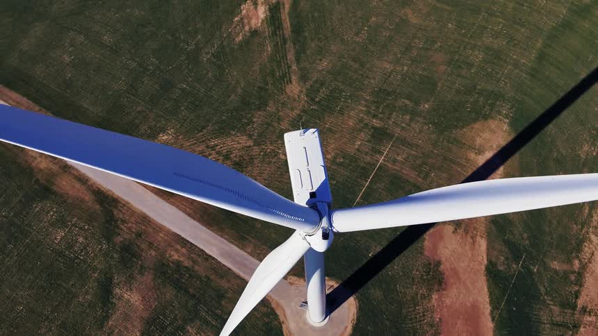 White wind turbine stands unmoving over green field casting long shadow