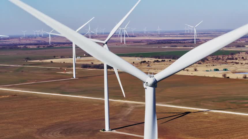 A wind turbine farm on a grassy plain with the sky and clouds in the background