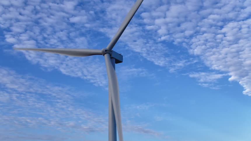 Wind turbine standing out against the blue sky spins around in the wind farm