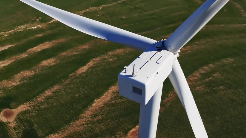 White wind turbine stands in green field bordered by roads and farmland