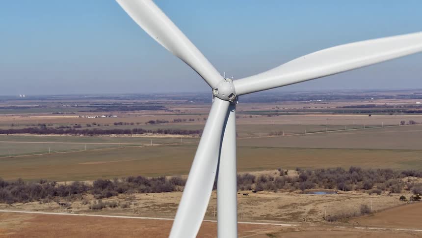 White wind turbine spins with fields and plains in background