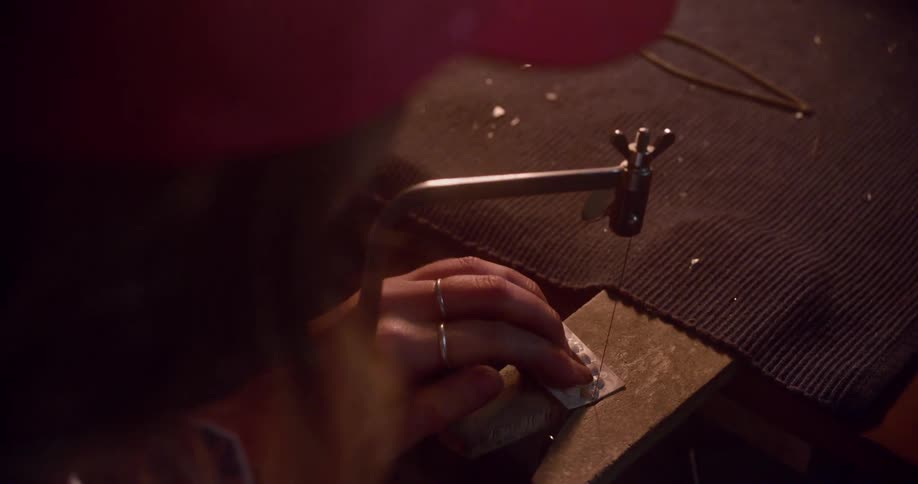 A woman uses a specialized tool with a thin metal wire to precisely cut through a small craft at her workbench