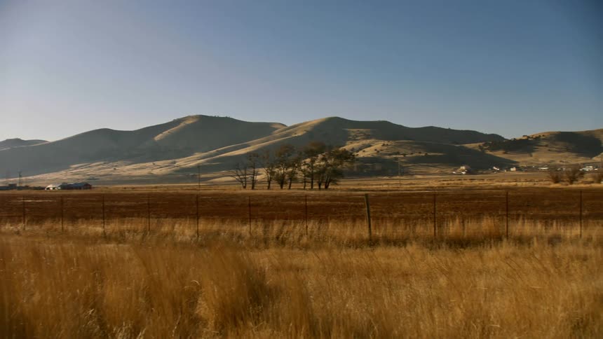 A countryside of yellowing grass with low mountains in the distance on a sunny day