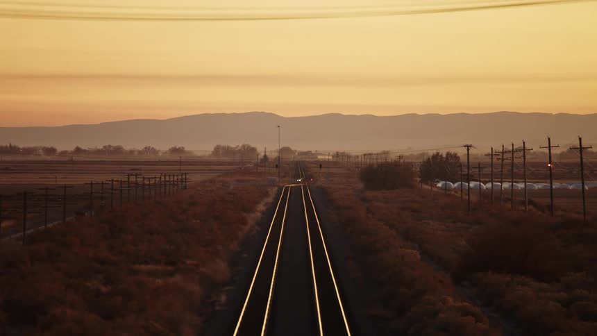 Distant cars drive over railroad tracks at sunset