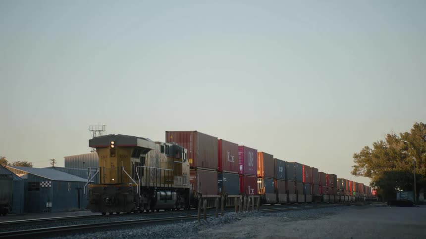 A cargo train moving on a train track with shipping containers with the sky and clouds in the background