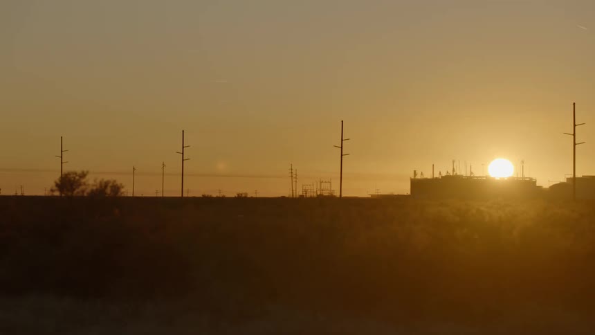 A grassy plain with utility poles trees the sky and the sun in the background