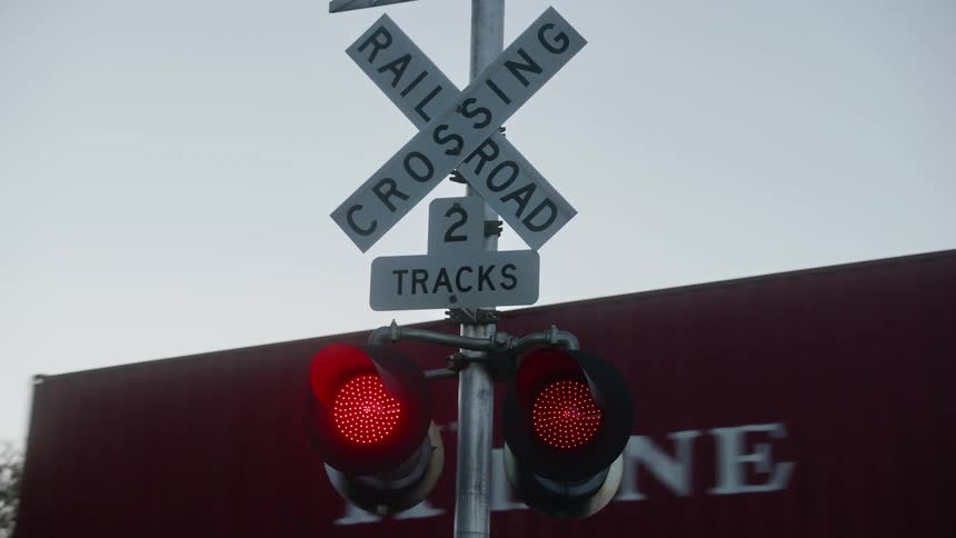 Train passes railroad crossing with blinking lights under clear sky