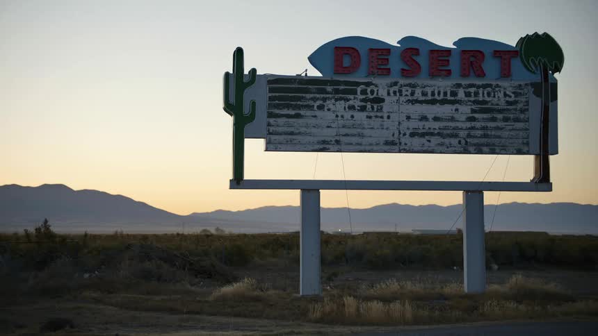 A sign in the desert with mountains the sky and clouds in the background