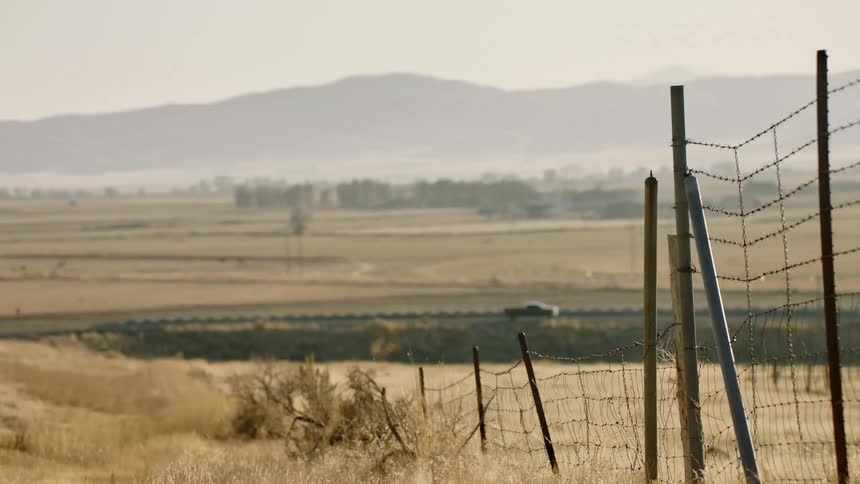 Vehicles travel along a road through a yellowing countryside