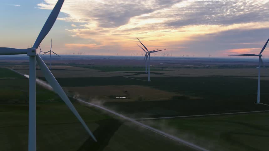 Wind turbines rotate in a rural field at sunset