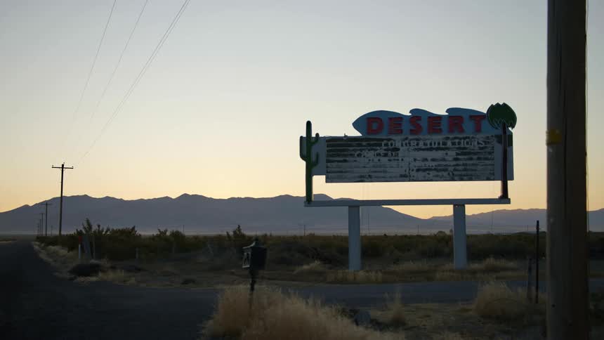 An abandoned and dilapidated sign stands along a dirt road that runs through a desert landscape