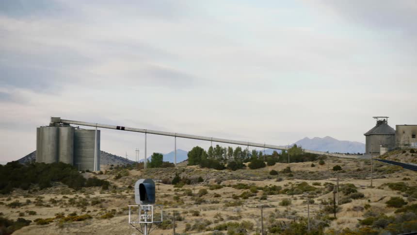 A set of large silos with a long connected chute stands in a rural area