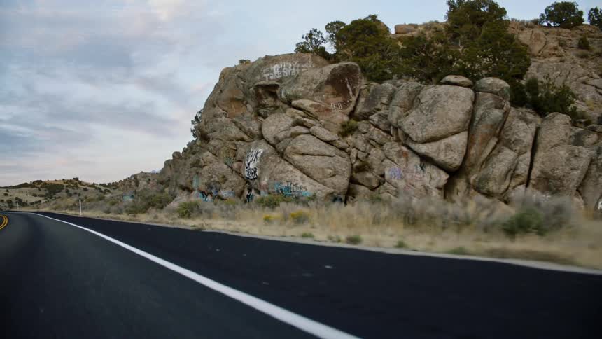 A road next to a rocky cliff with hills trees and the sky in the background